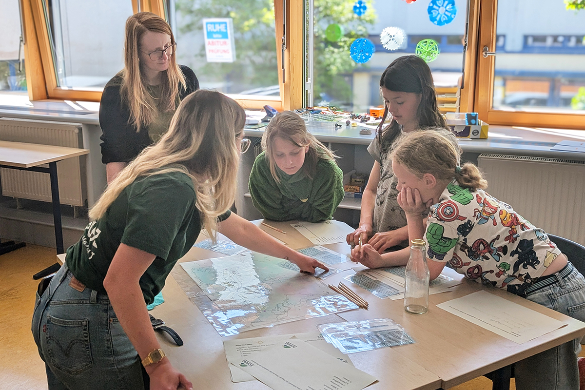 Rebecca Baumer (SCHUBZ) zeigt Patrizia Jäger (Lünestrom) und drei Kindern der IGS Lüneburg etwas auf den Arbeitsunterlagen.